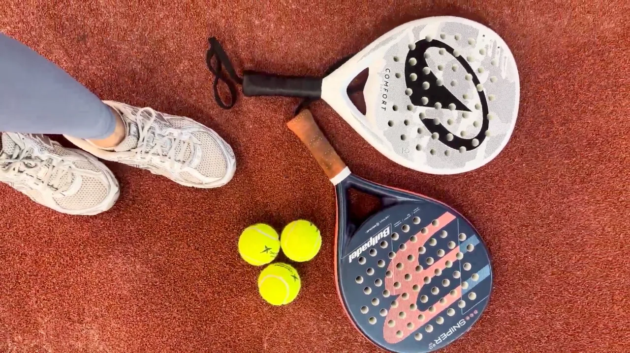 Raket dan bola padel di lantai lapangan.